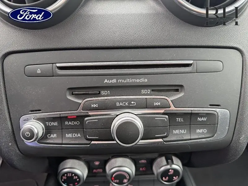 Vue rapprochée de la console centrale noire brillante de l'Audi A1 Sportback avec commandes multimédia et boutons de réglage.