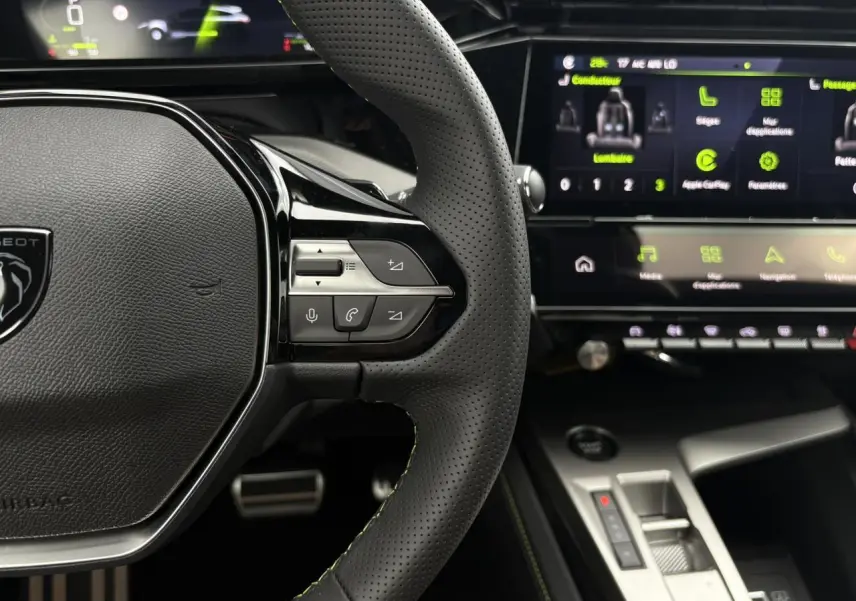 Gros plan sur le volant perforé noir avec surpiqûres vert Adamite et écran tactile du Peugeot 308 SW Hybrid 2026.