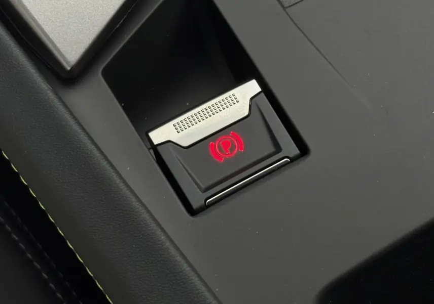 Gros plan sur le bouton de frein de parking électrique illuminé en rouge dans l'habitacle noir du Peugeot 308 SW Hybrid.