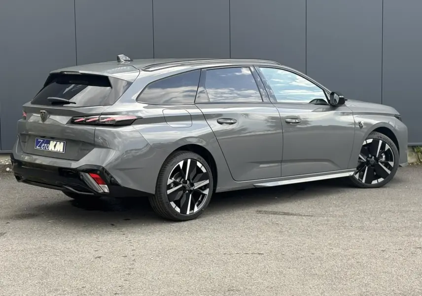 Peugeot 308 SW gris Sélénium vue 3/4 arrière droit, jantes alliage bicolores et barres de toit noires.