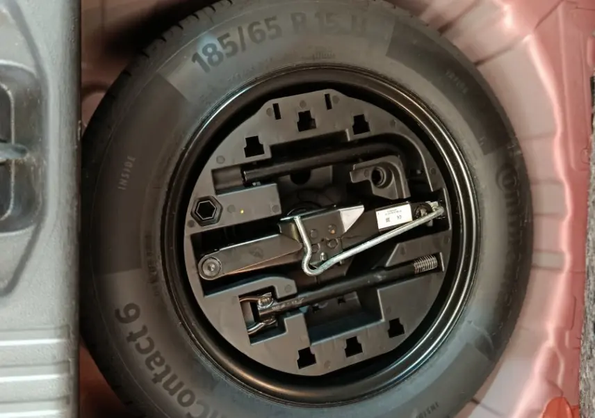 Vue plongeante sur la roue de secours noire et ses outils dans le coffre rouge de la Renault Clio Techno TCe 90 2024.