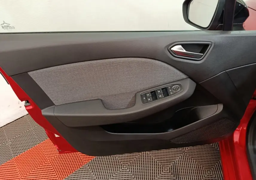 Vue intérieure de la porte avant gauche rouge de la Renault Clio 2024, avec commandes électriques et habillage tissu gris.