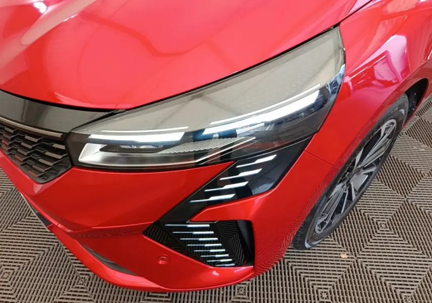 Gros plan sur l'avant droit de la Renault Clio Techno TCe 90 rouge, mettant en valeur son phare LED et la calandre noire.