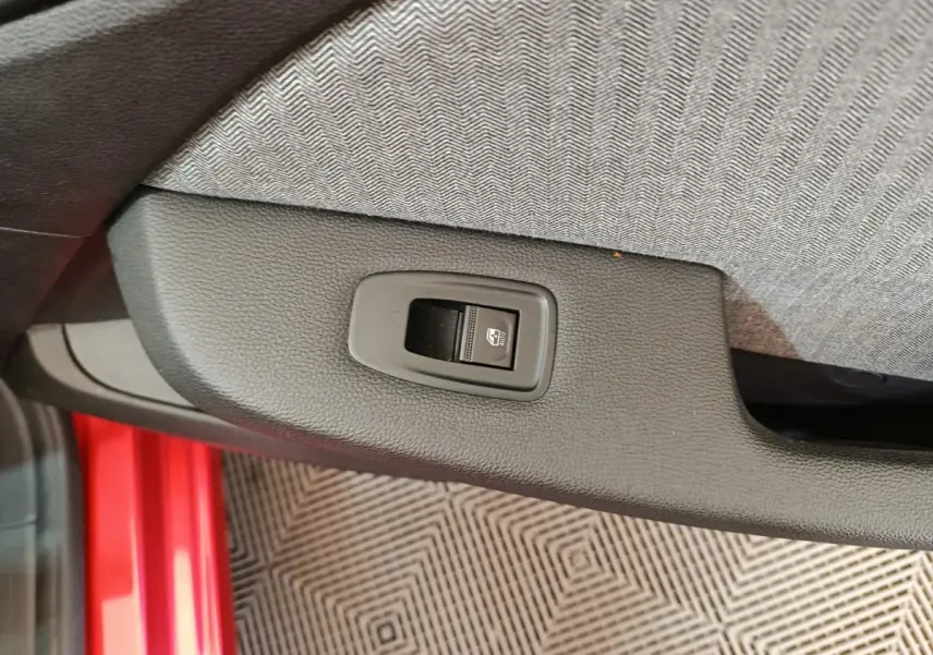 Gros plan sur le bouton de commande de lève-vitre côté conducteur, avec partie de la porte rouge visible.