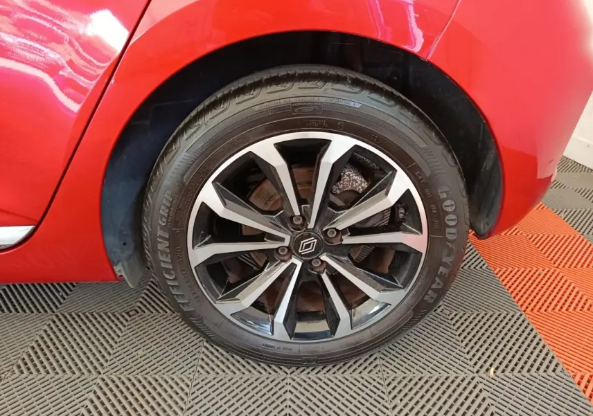 Gros plan sur la roue avant droite d'une Renault Clio rouge 2024 avec jante alliage bicolore et logo Renault au centre.