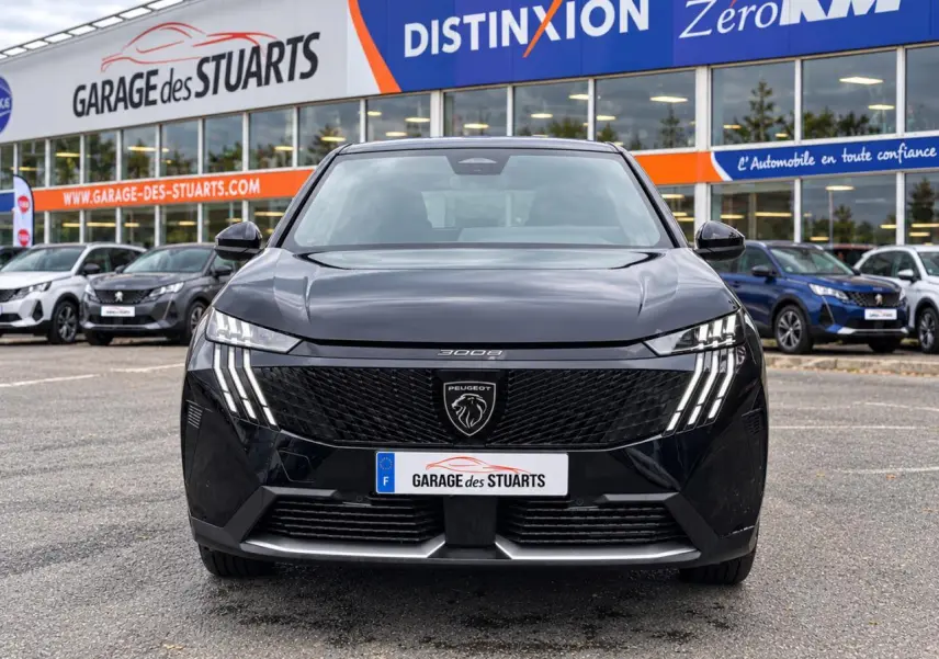 Vue avant d’un Peugeot 3008 noir Perla avec calandre noire et feux LED à griffes distinctifs, stationné devant un garage.