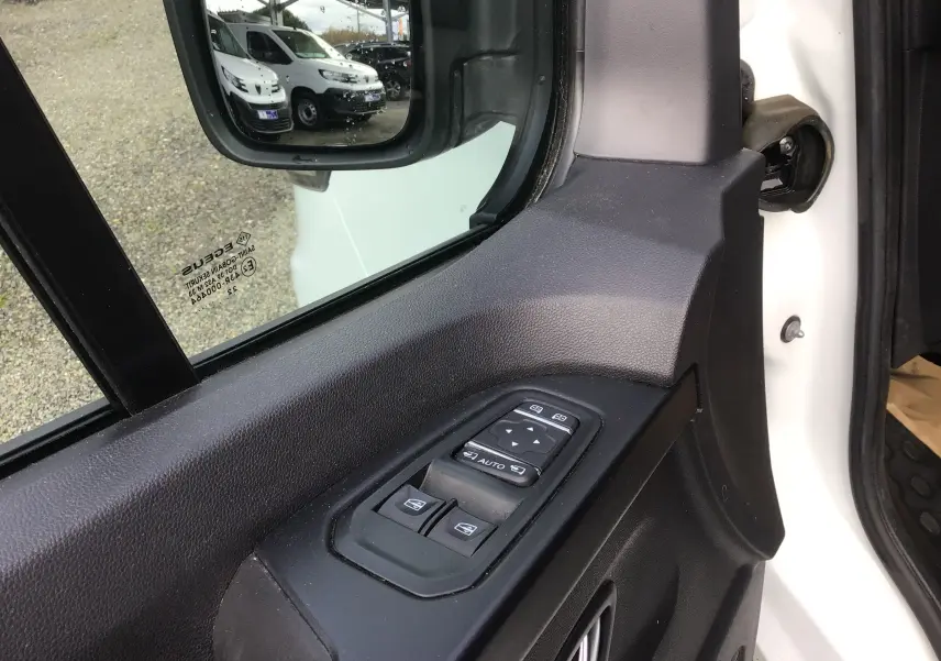 Gros plan sur la commande des vitres côté gauche d’un Renault Trafic Fourgon blanc, avec rétroviseur et reflet extérieur visibles.