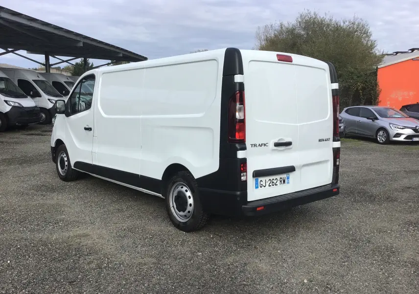 Renault Trafic Fourgon blanc vu en 3/4 arrière côté gauche, avec plaques françaises et détails noirs contrastants.