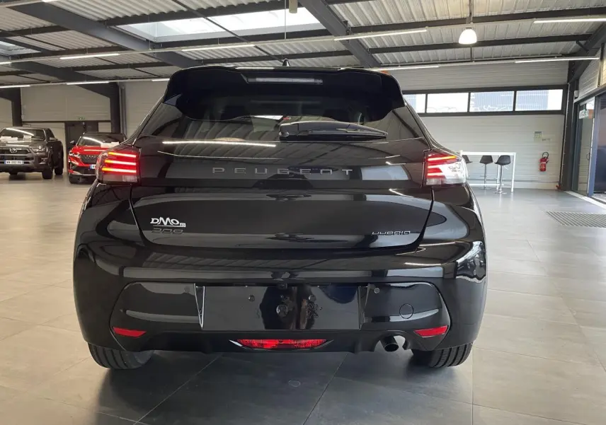 Vue arrière d'une Peugeot 208 noire avec feux arrière à LED et becquet noir brillant dans un garage.