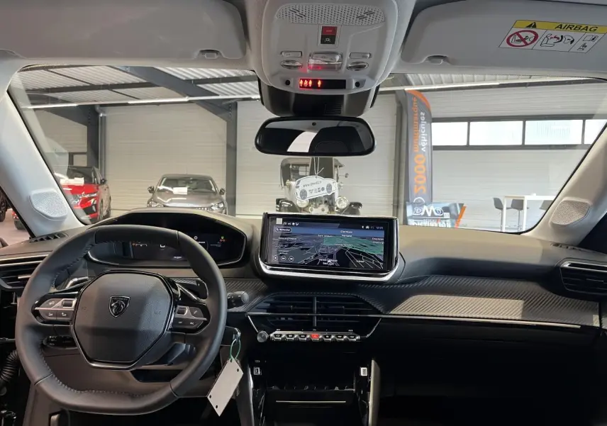 Vue intérieure avant du Peugeot 208 2025, tableau de bord noir avec écran tactile central et volant compact cuir.