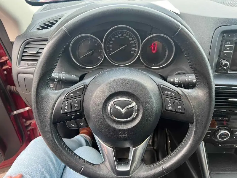 Vue intérieure centrée sur le volant cuir noir du Mazda CX-5 2013, avec tableau de bord et commandes visibles.