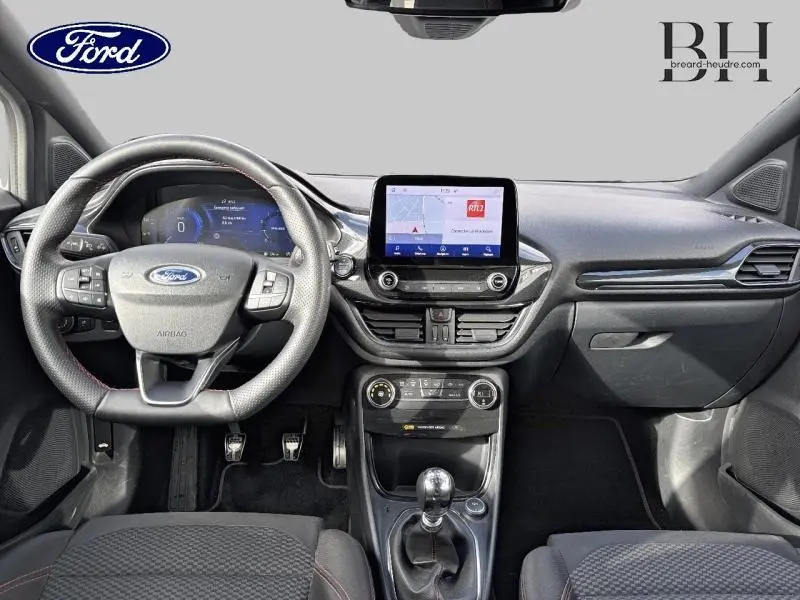 Vue intérieure frontale du tableau de bord et volant cuir noir du Ford Puma blanc avec écran tactile central et levier de vitesses manuel.