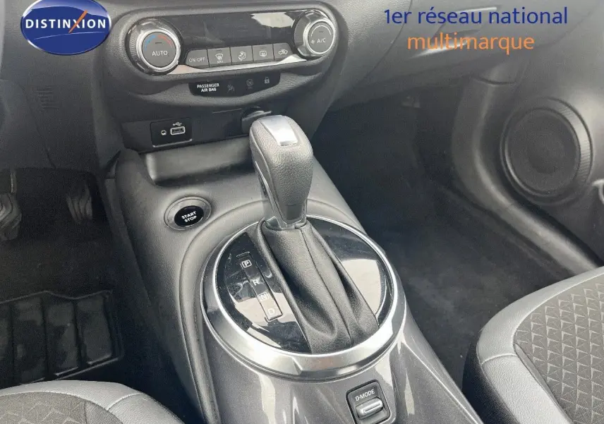 Gros plan sur la console centrale du Nissan Juke blanc nacré 2024, mettant en valeur le levier de vitesse automatique et les commandes climatiques.