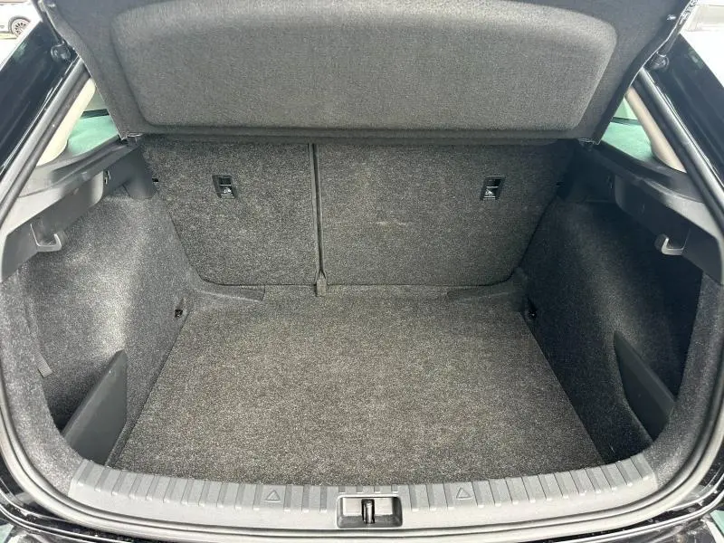 Vue intérieure du coffre ouvert d'une SKODA SCALA noir Magic nacré, montrant un espace de rangement propre et tapissé de moquette grise.