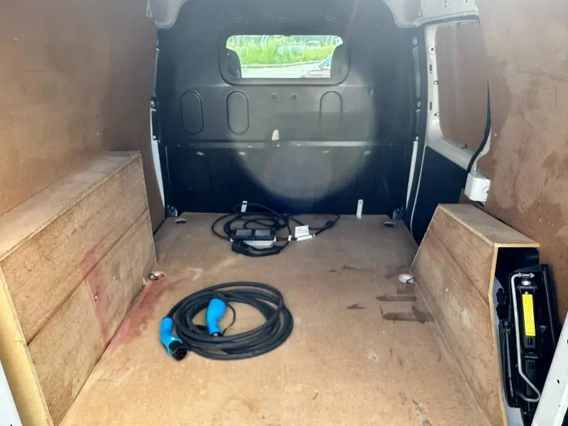 Vue intérieure du coffre du Renault Kangoo Express blanc minéral, montrant un câble de recharge électrique et un espace de chargement vide.