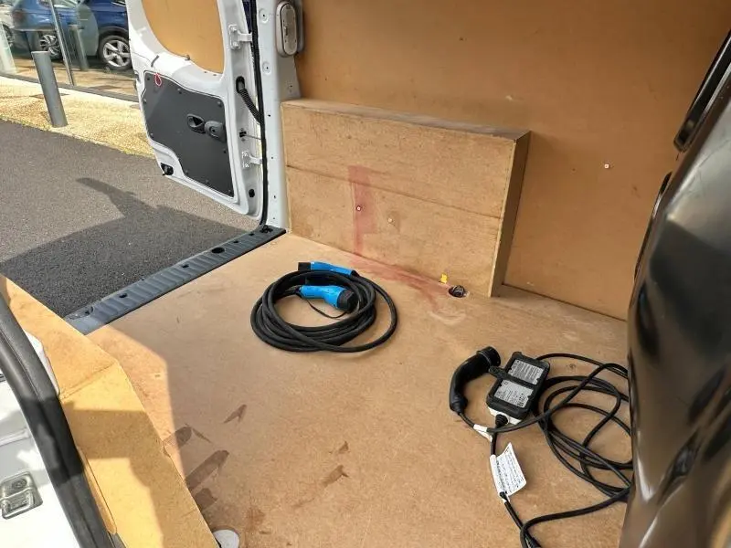 Vue intérieure arrière du Renault Kangoo Express blanc minéral, montrant le plancher en bois et les câbles de recharge électrique.