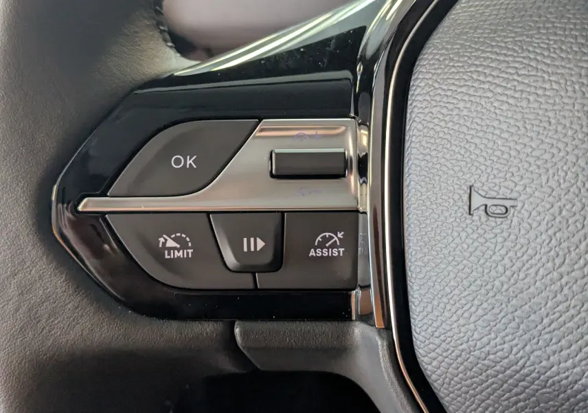 Gros plan sur les commandes au volant à gauche du Peugeot Rifter gris Artense, avec boutons OK, limiteur et assist.