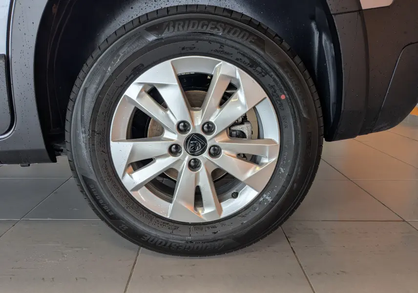 Gros plan sur la roue avant droite du Peugeot Rifter gris Artense 2025 avec jante alliage 16 pouces et logo lion central.