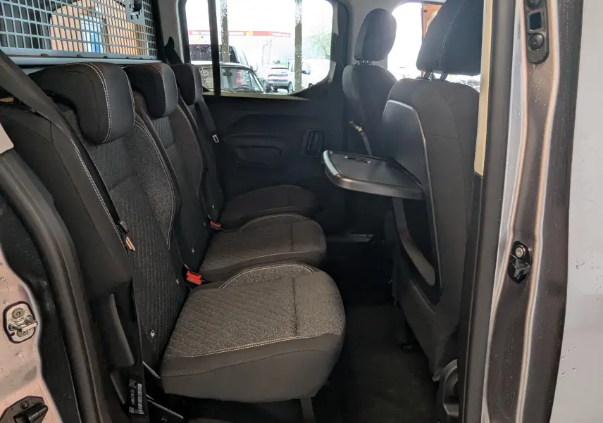 Vue intérieure côté droit des sièges arrière en tissu gris du Peugeot Rifter 2025, avec tablette rabattable sur le dossier avant.