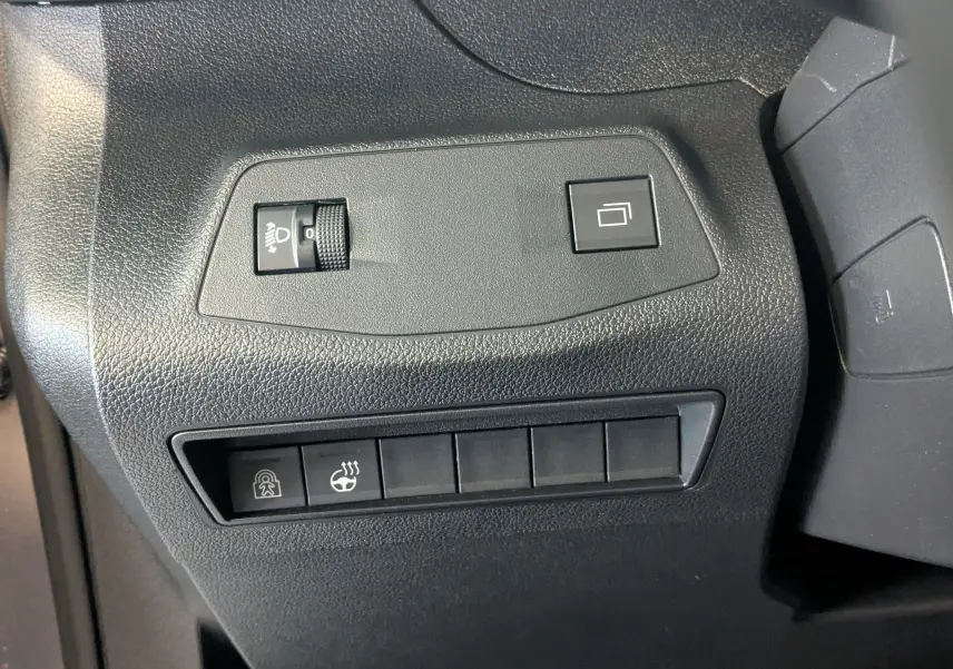 Vue rapprochée des commandes noires sur tableau de bord du Peugeot Rifter gris Artense, incluant réglage phares et siège chauffant.