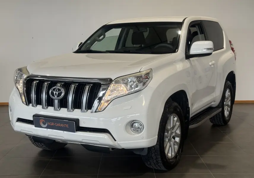 Toyota Land Cruiser blanc en 3/4 avant droit, mettant en valeur sa calandre chromée et ses phares allumés.