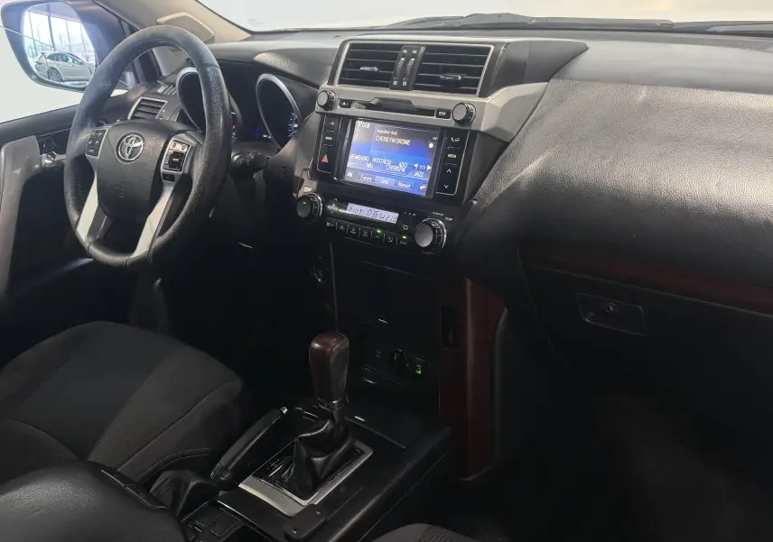 Vue intérieure côté conducteur du Toyota Land Cruiser 2.8 D-4D 2015, tableau de bord noir avec écran tactile et levier de vitesse automatique.