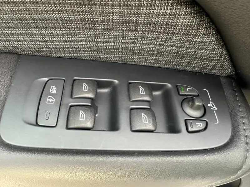 Gros plan sur les commandes de lève-vitres et réglage des rétroviseurs côté conducteur du Volvo XC60 blanc cristal métallisé 2024.