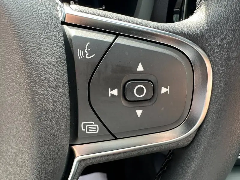 Gros plan sur les commandes vocales et de navigation au volant noir du Volvo XC60 blanc cristal métallisé 2024.