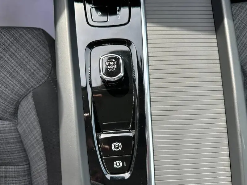 Gros plan sur la console centrale noire brillante du Volvo XC60 2024 avec bouton Start Engine Stop et commandes de frein à main.