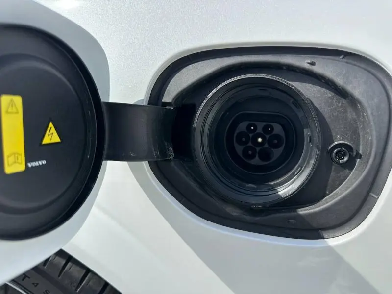 Prise de recharge hybride ouverte côté gauche sur Volvo XC60 blanc cristal métallisé, avec avertissements visibles sur le cache.