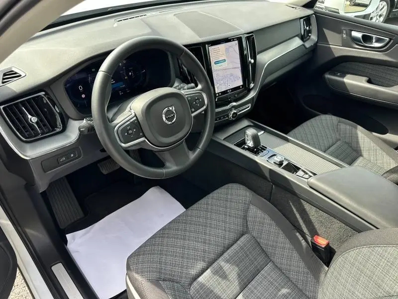Vue intérieure côté conducteur du Volvo XC60 2024, tableau de bord noir avec écran tactile vertical et sièges tissu gris à motifs.