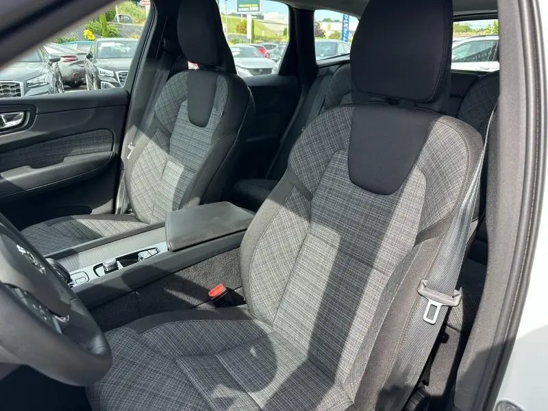 Vue intérieure côté conducteur du Volvo XC60 blanc, sièges tissu gris à motif carreaux avec appuie-tête noir.
