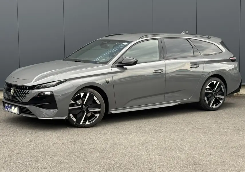 Peugeot 308 SW gris Sélénium vue 3/4 avant droit avec jantes bi-tons et barres de toit noires.