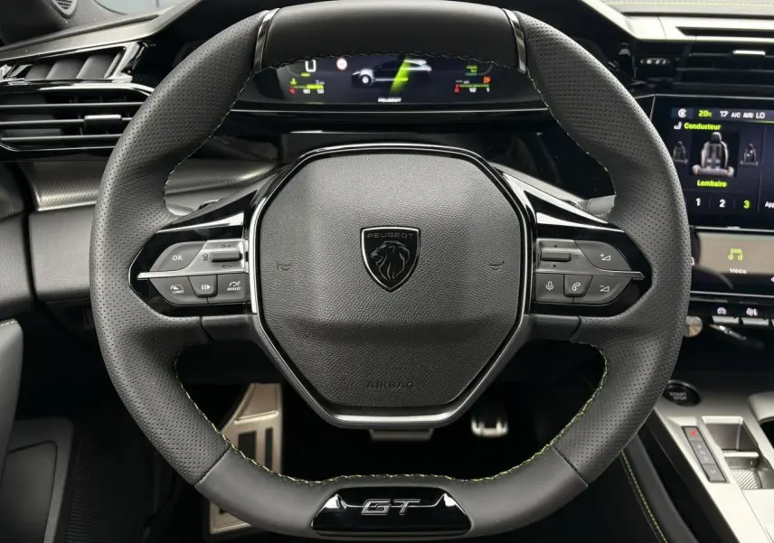 Vue rapprochée du volant compact GT en cuir noir avec surpiqûres vert Adamite du Peugeot 308 SW Hybrid 2026.