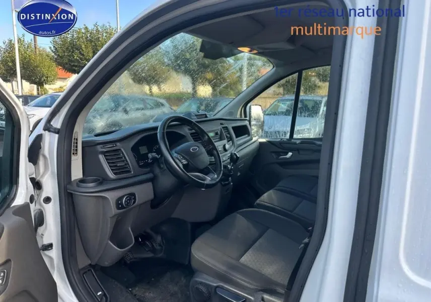 Vue intérieure côté conducteur du Ford Transit Custom blanc de 2021, montrant le tableau de bord et les sièges noirs.