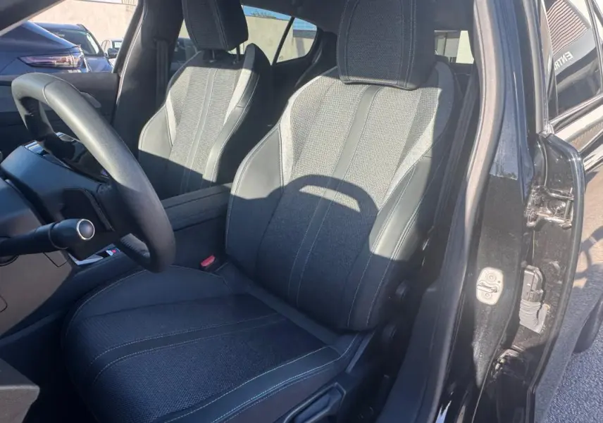 Vue intérieure côté conducteur de la Peugeot 408 Hybrid 145 Allure 2025 noire, mettant en valeur les sièges en tissu et cuir.