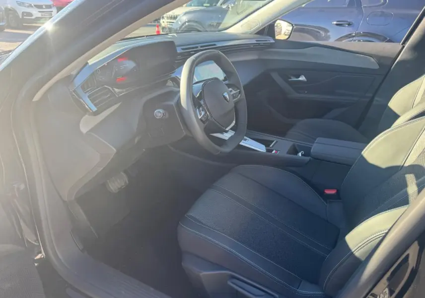 Vue intérieure côté conducteur du Peugeot 408 Hybrid 145 e-DCS6 Allure 2025, sièges noirs et tableau de bord moderne.
