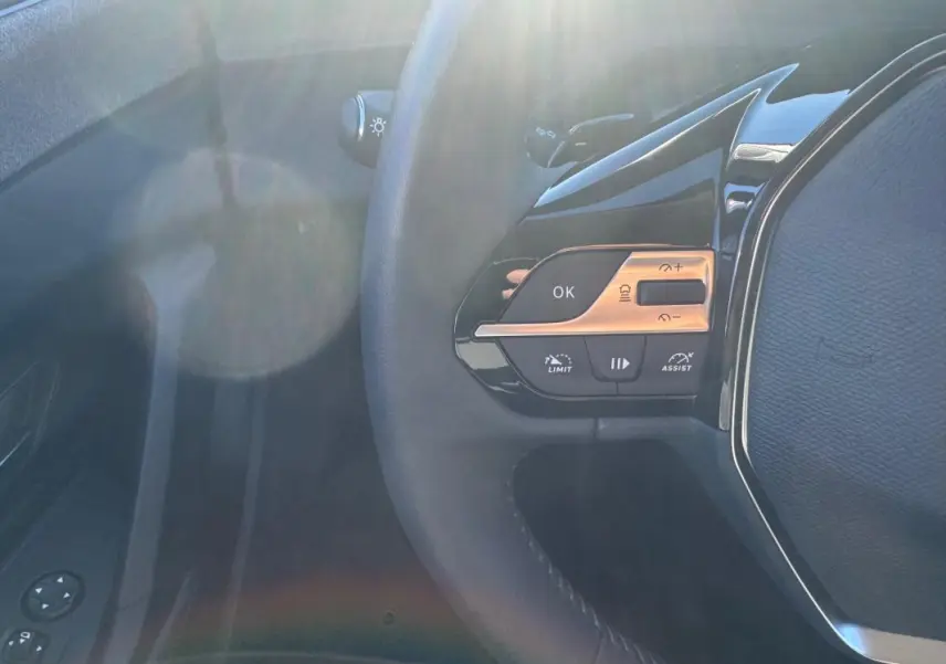 Gros plan sur les commandes à gauche du volant noir du Peugeot 408 Hybrid 145 e-DCS6 Allure 2025, avec boutons multifonctions.