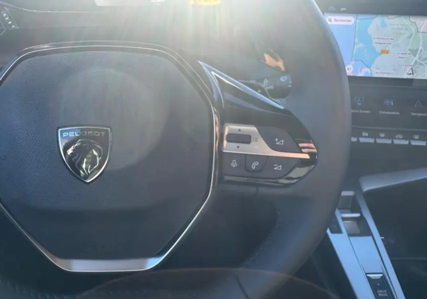 Vue rapprochée du volant noir de la Peugeot 408 Hybrid 145 e-DCS6 Allure 2025 avec commandes intégrées et écran tactile visible.