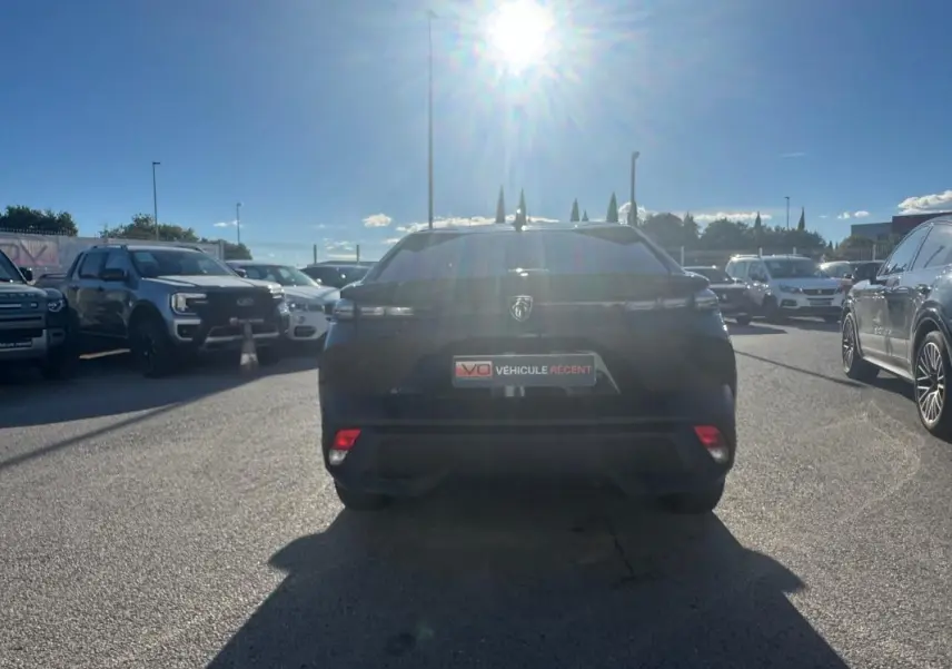 Vue arrière d'une Peugeot 408 Hybrid 145 e-DCS6 Allure noire 2025, stationnée en extérieur sous un soleil éclatant.