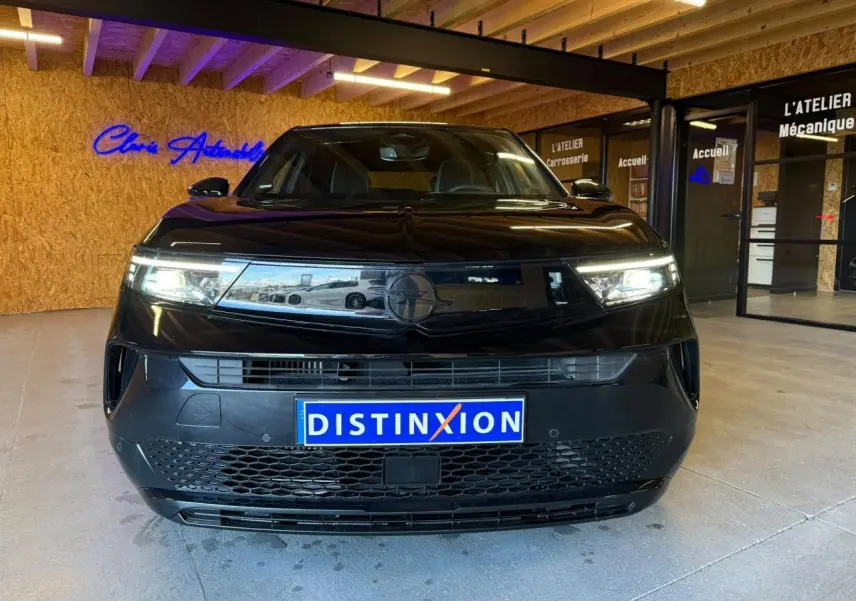 Vue avant d’un Opel Mokka noir 2025 avec calandre Vizor et phares LED allumés en intérieur showroom.