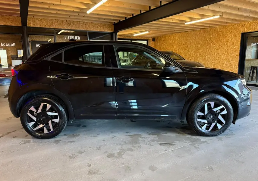Opel Mokka noir vue de profil côté gauche, avec jantes alliage diamantées et vitres surteintées en intérieur d'atelier.