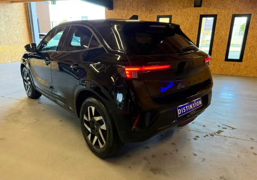 Opel Mokka noir vue 3/4 arrière droit en intérieur, feux arrière LED allumés et jantes alliage 17 pouces.