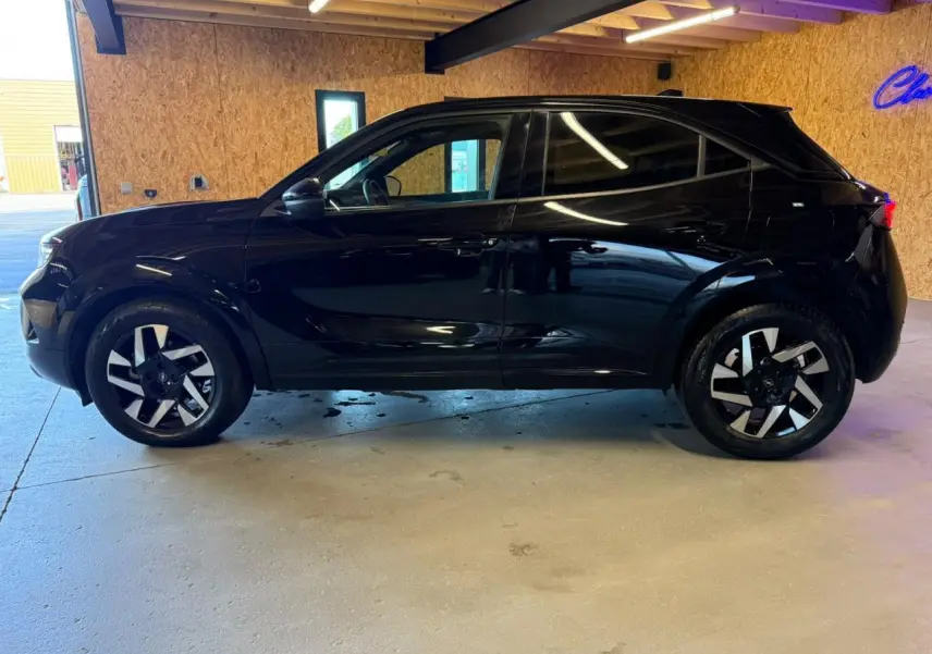 Profil côté gauche d’un Opel Mokka noir métallisé 2025 avec jantes alliage 17 pouces diamantées, garé en intérieur.