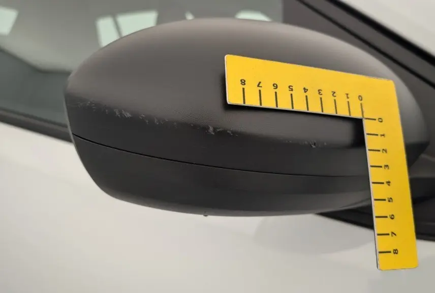 Gros plan sur le rétroviseur côté gauche noir mat de la Dacia Sandero blanche 2022 avec rayures visibles.