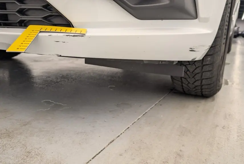 Gros plan sur l'angle avant droit d'une Dacia Sandero blanche avec rayures visibles sur le pare-chocs inférieur.