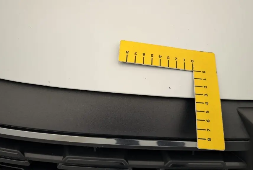 Gros plan sur le capot blanc glacier et la calandre noire d'une Dacia Sandero Eco-G 100 2022 avec un outil de mesure jaune posé dessus.