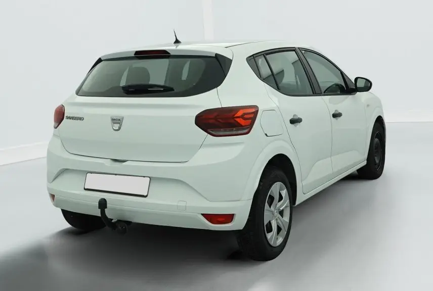Vue 3/4 arrière droite d'une Dacia Sandero blanche avec feux arrière LED et attelage de remorque visible.
