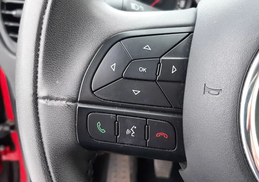 Gros plan sur les commandes au volant côté gauche du FIAT 500X rouge, avec boutons de navigation et appels intégrés.