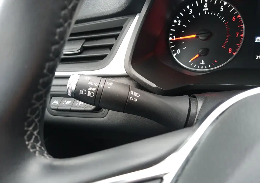 Gros plan sur le commodo des feux à gauche du volant dans l'habitacle noir du Renault Captur 2021 essence.